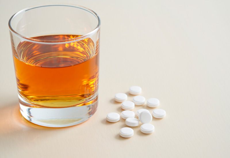 Стакан янтарного алкоголя и рассыпанные белые таблетки на тёмной глянцевой поверхности
